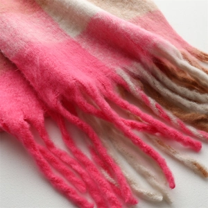 Close-up of thick knitted plaid scarf with soft tassels in rose pink and beige