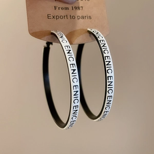 Détail de grandes boucles d'oreilles créoles avec lettres ENIC et contraste noir et blanc