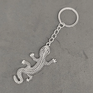 Detailed top view of a silver-toned metal gecko keychain on a gray textured background