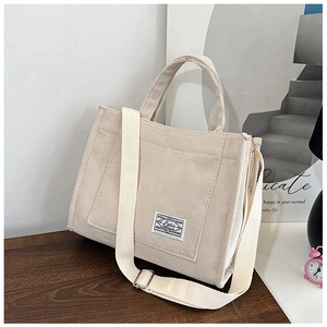 Off-white corduroy tote bag with adjustable shoulder strap on a dark wooden surface
