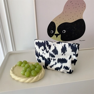 Detail of a cow print cotton makeup bag with black zipper and minimalist brand label
