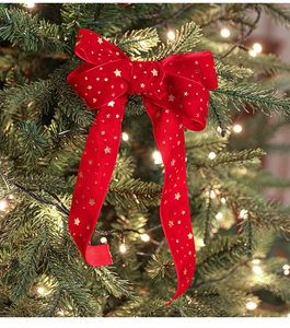 Close-up of red velvet Christmas bow with gold stars hanging on a festive lighted tree