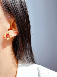 Close-up of white enamel flower earring featuring yellow petals and a red core on ear