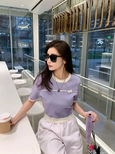 Close-up of a purple short-sleeved knit top with white trim and a delicate bow detail