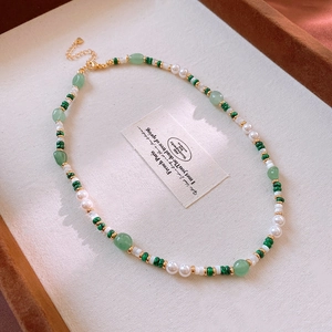 Detail of beaded necklace with green stone beads, pearls and gold spacers on beige tray