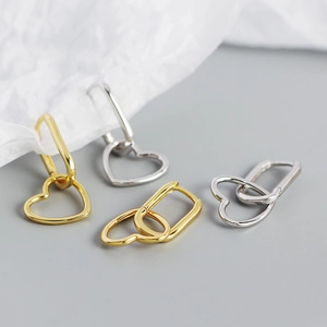 Detailed close-up of gold and silver S925 heart pendant hoop earrings on a grey background