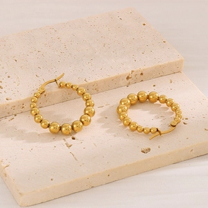 Detailed view of gold stainless steel beaded C-shaped earrings on stone surface