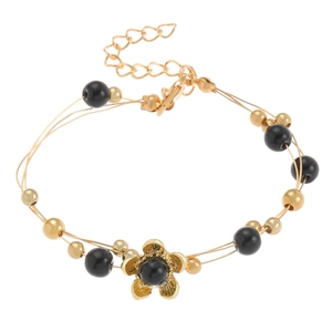 Detalle de la pulsera de hilo dorado de tres capas con cuentas negras y dije de flor