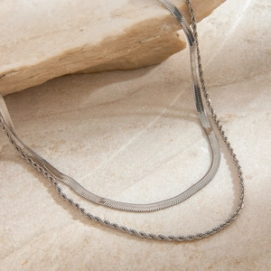Detailed view of silver flat snake chain and twisted rope necklaces on stone