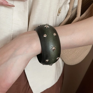 Détail d'un bracelet large vert foncé avec rivets étoiles et points argentés sur un mannequin