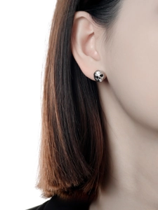 Close-up of a punk-style skull stud earring worn by a model to show refined metallic texture