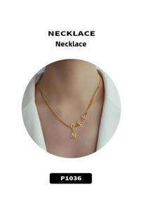 Close-up of golden necklace with hanging M-O-R-E letter charms worn on a white suit