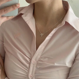 Close-up of elegant gold bow pendant necklace worn by a model on a pink shirt