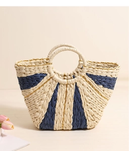 Detail of straw tote bag featuring navy stripes, gold threads, and round woven handles