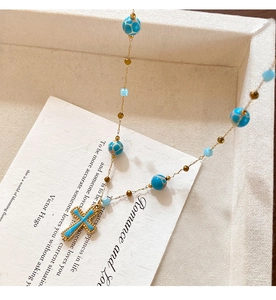 Detail of blue stone cross pendant necklace on a cream fabric jewelry gift box