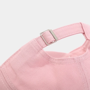 Detail of pink cotton baseball cap featuring adjustable silver metal buckle and clean stitching