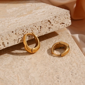 Macro shot of gold-plated pear-shaped earrings on stone and silk background