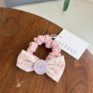Detail of pink floral bow hair scrunchie with pearl-rimmed letter A emblem on wood