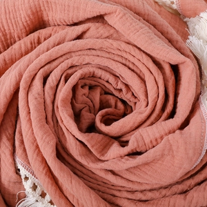 Terracotta muslin baby blanket with white lace tassel fringe edge in spiral display