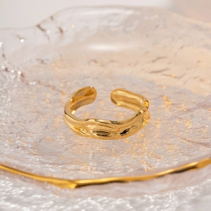 Detail shot of a wavy textured 18k gold plated adjustable ring on a glass tray