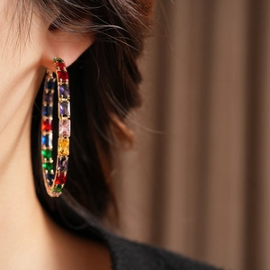 Detail of colorful rectangular zircons on large golden hoop earrings worn by a model
