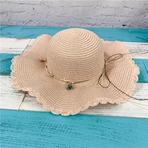 Detail of pink straw sun hat featuring wavy brim and decorative floral pendant tassels