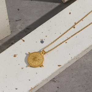 Collier avec pendentif boussole solaire en acier doré sur une surface en pierre moderne