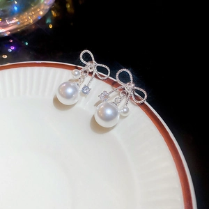 Detail of silver bow earrings with pearls and cubic zirconia on a white ceramic plate