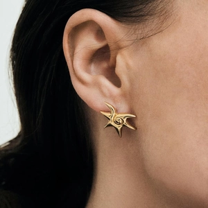 Close-up of gold star earring with swirl texture on a model's ear, sleek steel jewelry