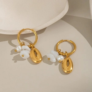 Détail de créoles dorées avec perles naturelles et pendentifs coquillages sur fond beige