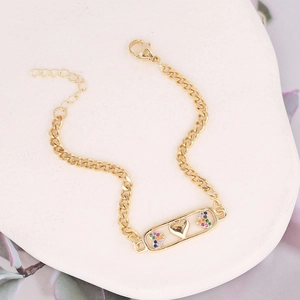 Detail of gold star and rainbow heart bracelet with zircons on a white stone background