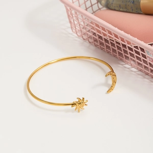 Détail d'un bracelet ouvert en or 18K avec breloques soleil et lune sur fond blanc