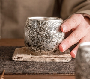Gros plan d'une tasse en argent 999 avec gravure de dragon tenue dans la main