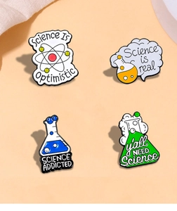 Close-up of science enamel pins featuring atom symbols and chemical beakers with text