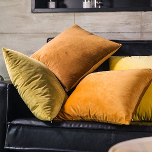 Stack of four solid velvet pillow covers in brown, yellow, orange and green on a leather sofa