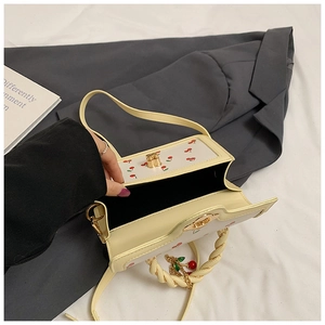 Detail view of cream rectangle bag featuring cherry prints and gold metal twist lock