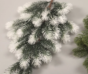 Close-up of artificial pine branch with green needles and realistic white snow flocking