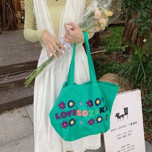 Close-up of green canvas tote bag featuring 3D floral embroidery and artistic lettering
