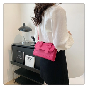 Detail view of a bright pink PU leather crossbody bag with buckle straps worn by a model