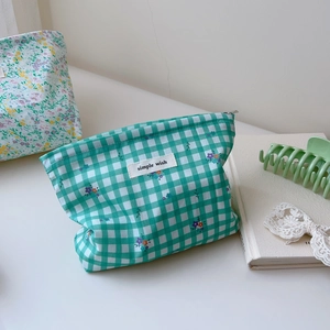 Detail of green plaid makeup bag with floral print and zipper closure on a white desk
