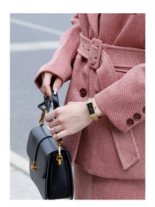 Close-up of elegant gold rectangular watch with black dial and mesh strap on female wrist