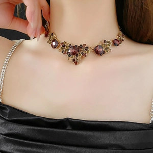 Detail of vintage gold leaf necklace with deep red gemstones on a model's neck