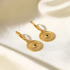 Macro shot of gold-plated evil eye hoop earrings with green gemstone on silk