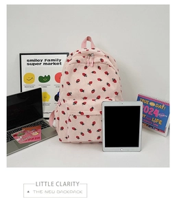 Pink corduroy backpack with red strawberry patterns on desk with laptop and tablet