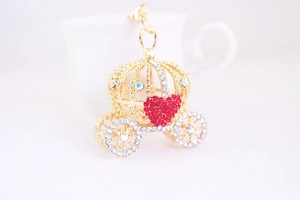 Détail d'un porte-clés carrosse citrouille doré avec cœur rouge et strass brillants décorés