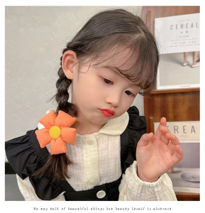 Close-up of a cute orange sunflower hair tie on a little girl's braided hairstyle