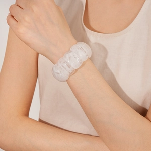 Close-up of a wide geometric white acrylic stretch bracelet worn by a model in warm light