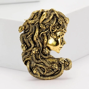 Vintage gold Medusa head brooch with detailed carving on a white geometric background