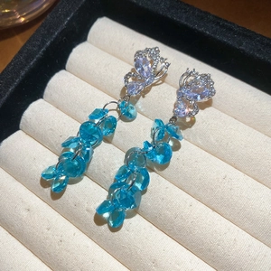 Gros plan de boucles d'oreilles papillon à pompons et cristaux bleus en écrin blanc