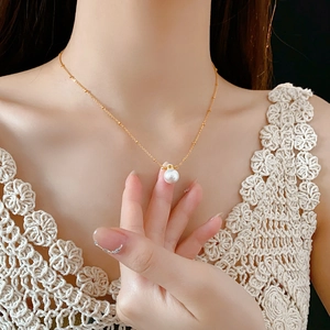 Detail of elegant gold necklace featuring a single white pearl on a model neck